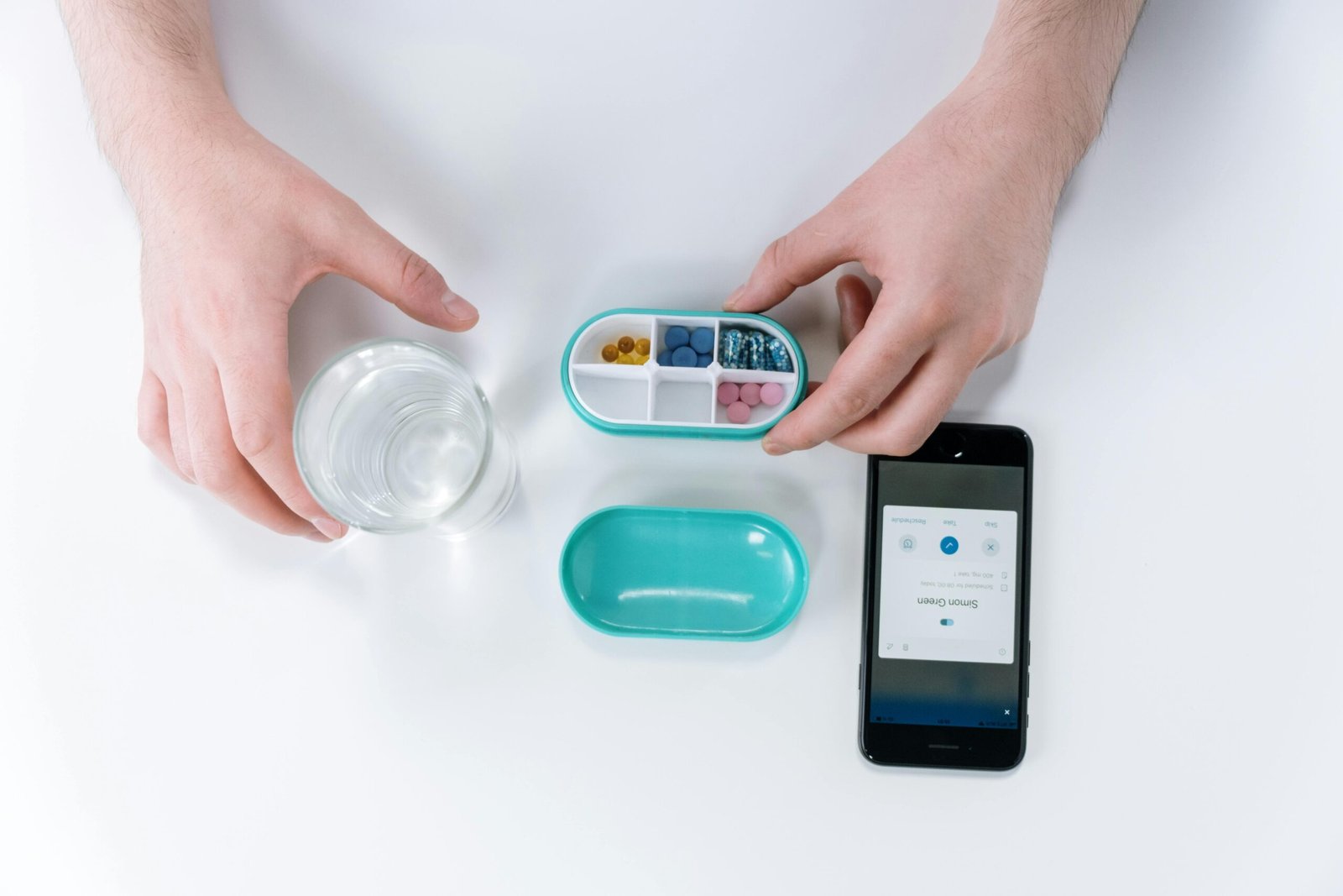 Overhead view of hands using a smartphone app and pill organizer for medication management.